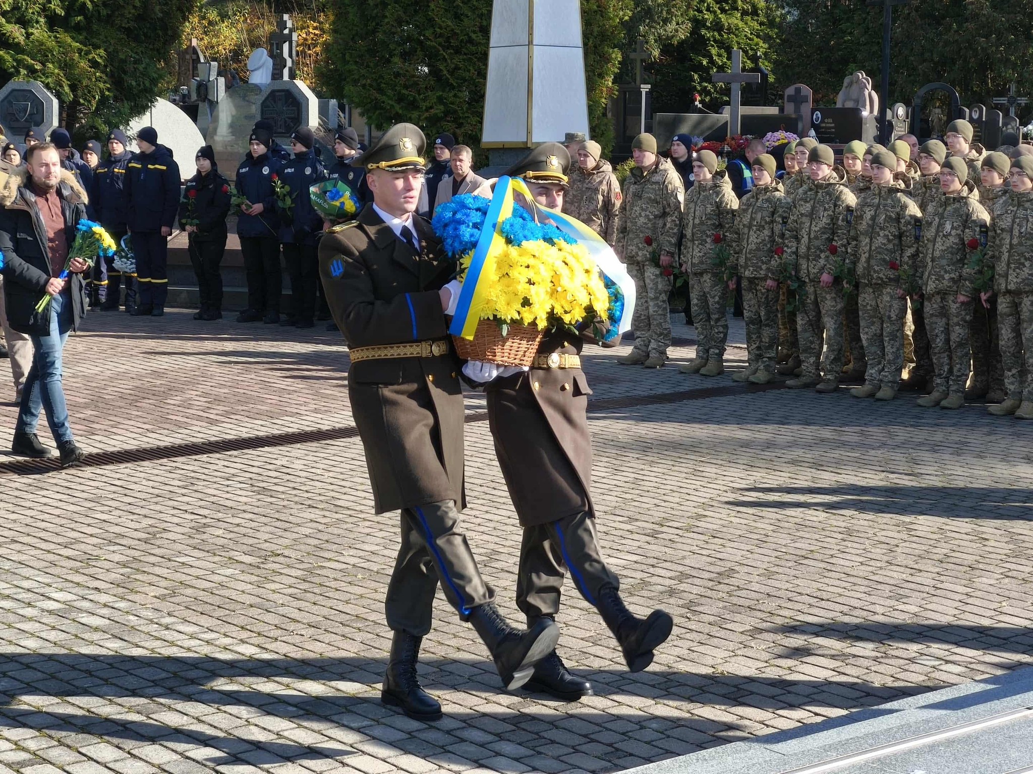 військовослужбовці несуть синьо-жовтий букет, на фоні стоїть юрба людей