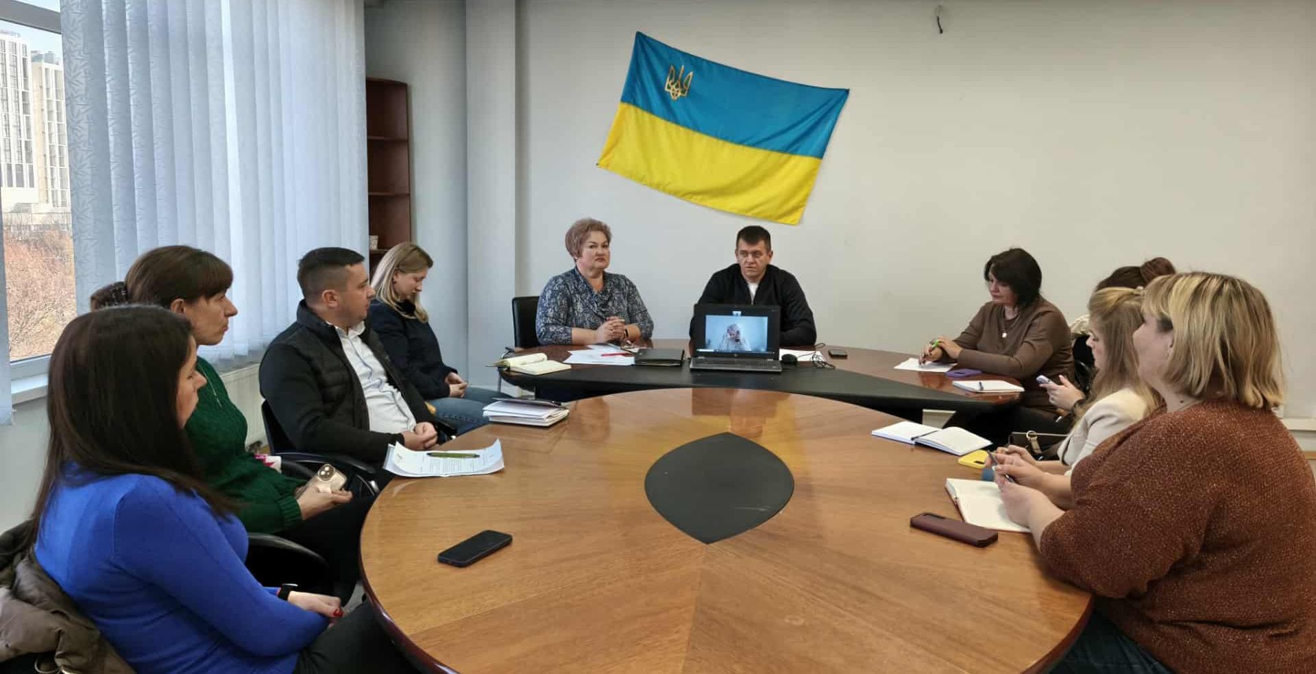 люди сидять на нараді, синьо-жовтий прапор на стіні