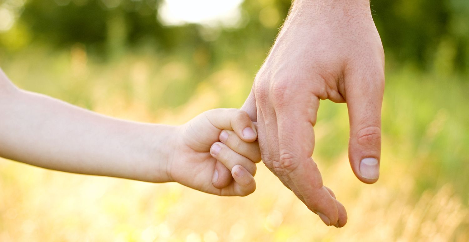 дитяча рука тримається за мізинець дорослої чоловічої руки на фоні зеленої природи