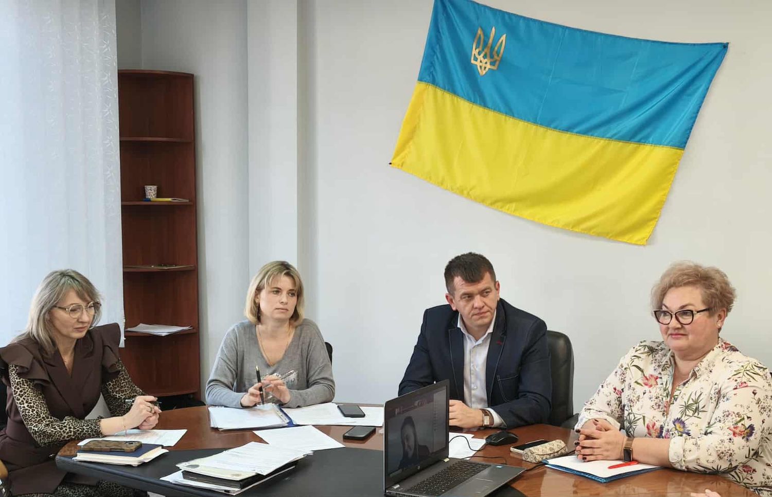 люди сидять столом, на задньому фоні на стіні висить синьо-жовтий прапор