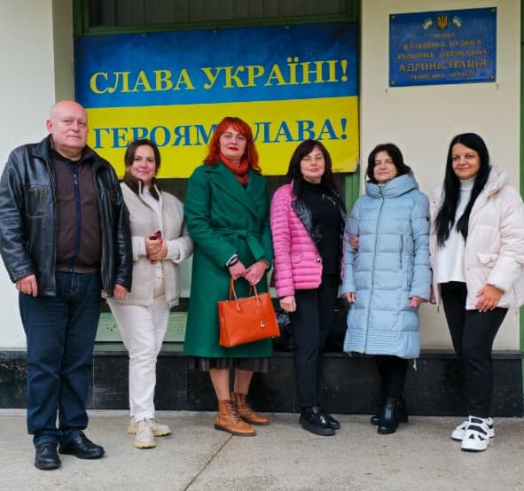 люди стоять на фоні будівлі з написом "СЛАВА УКРАЇНІ! ГЕРОЯМ СЛАВА!"