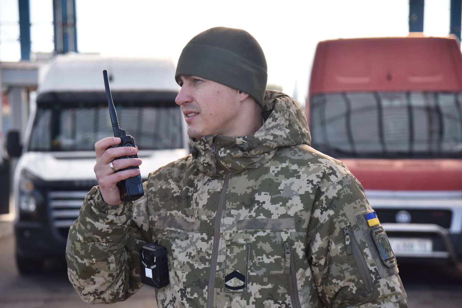 прикордонник з рацією на фоні двох бусів
