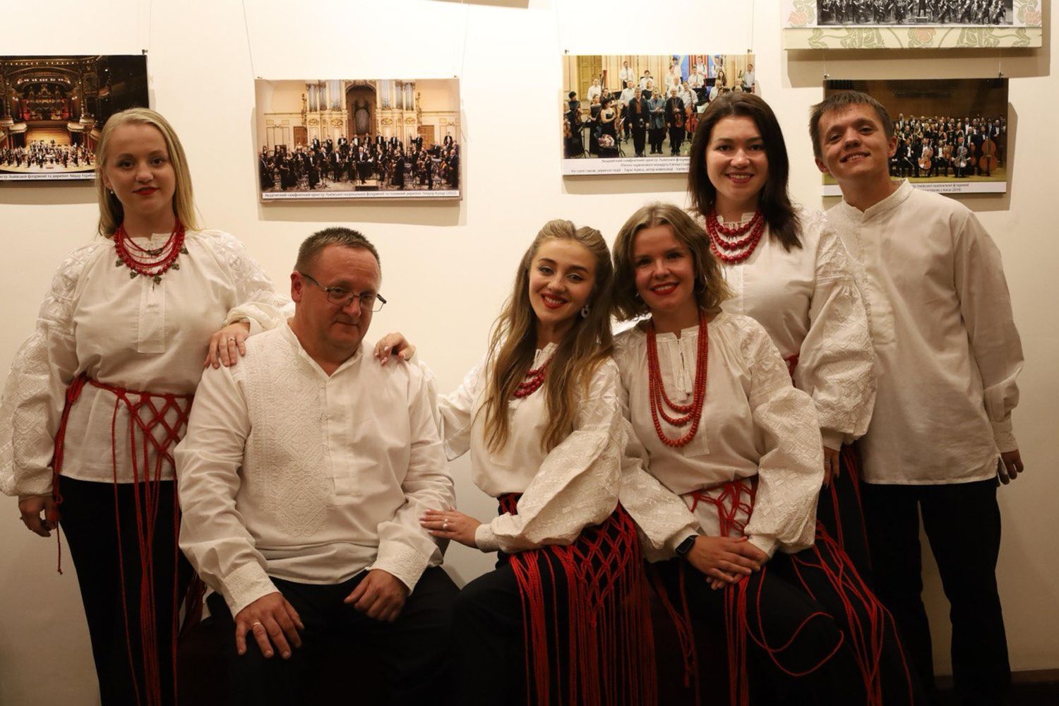 два чоловіка та чотири жінки на фоні білої стіни з картинами