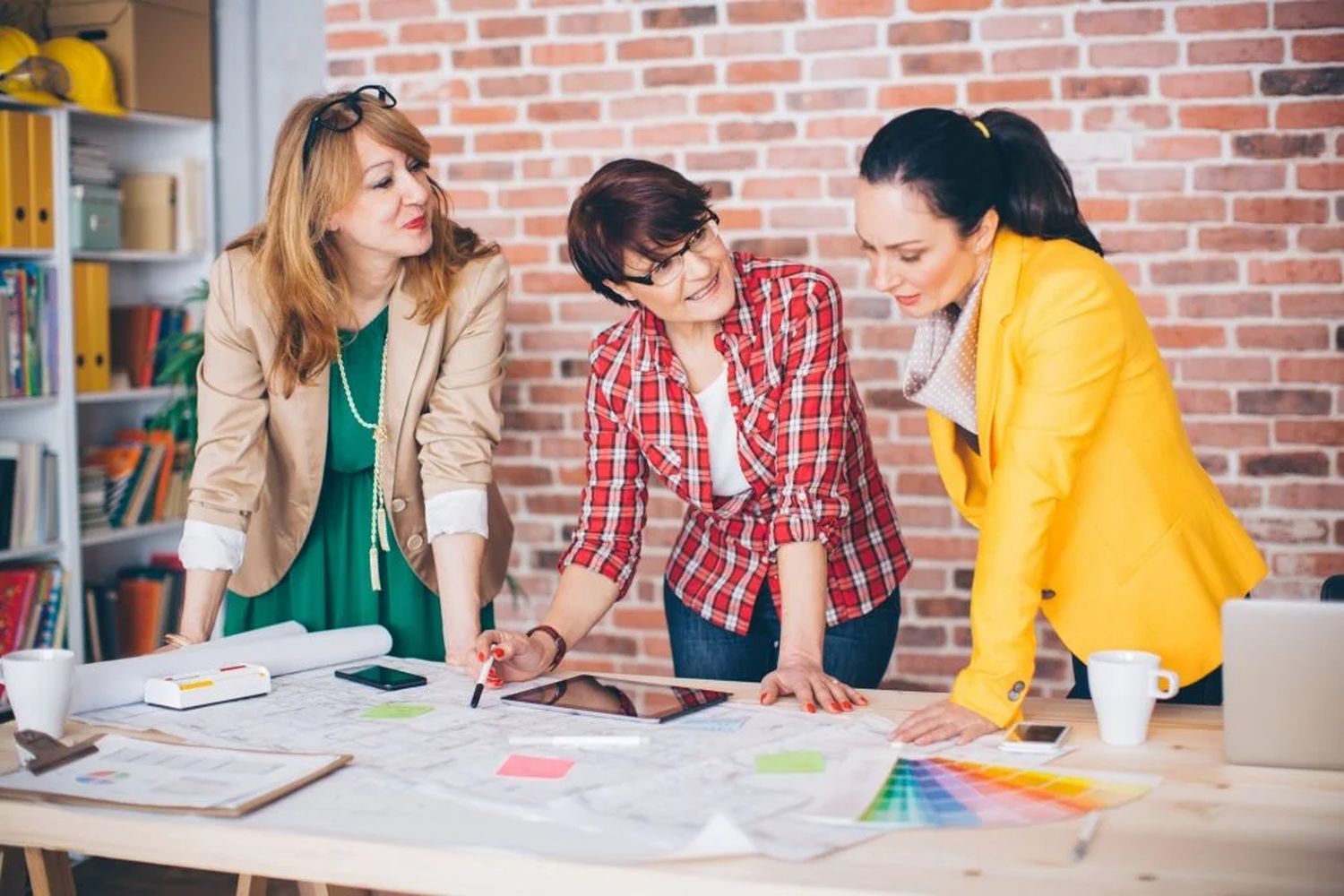 три жінки стоять в кімнаті над столом з кресленнями