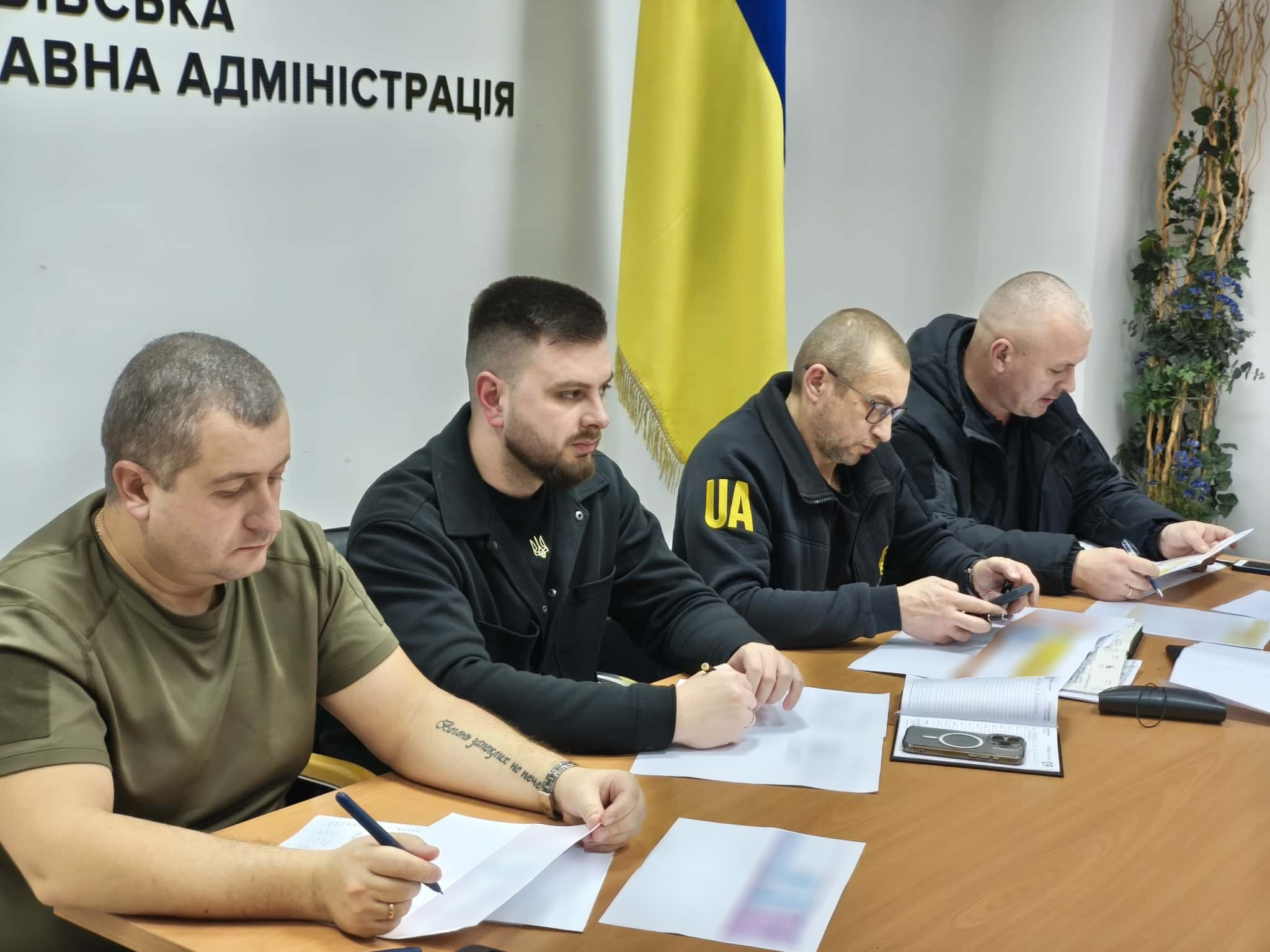 люди сидять за столом, на фоні український прапор і напис "АДМІНІСТРАЦІЯ"