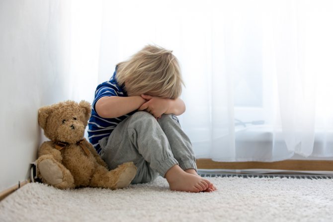 дитина закрила обличчя руками, поруч плюшевий ведмедик