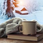 чашка, книжка та шафр на підвіконні, за вікном – будинов та ялина під снігом